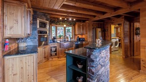 Cocina de cabaña de madera con detalles de piedra, electrodomésticos integrados y una isla de piedra.