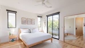 Un dormitorio moderno con una cama grande, un ventilador de techo y un ventanal corredero que da a un balcón.