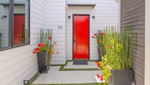 Una casa moderna con puerta roja, número 723, y un pequeño jardín delantero con plantas en macetas y césped.
