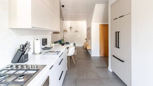 Una cocina moderna con muebles blancos, una estufa a gas y un comedor con mesa y sillas blancas.