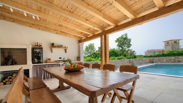 Un patio al aire libre con una mesa y bancos de madera, una piscina y un muro de piedra.