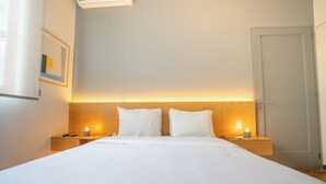 A neatly made bed with white linens, two bedside tables with lamps, and a wooden headboard.