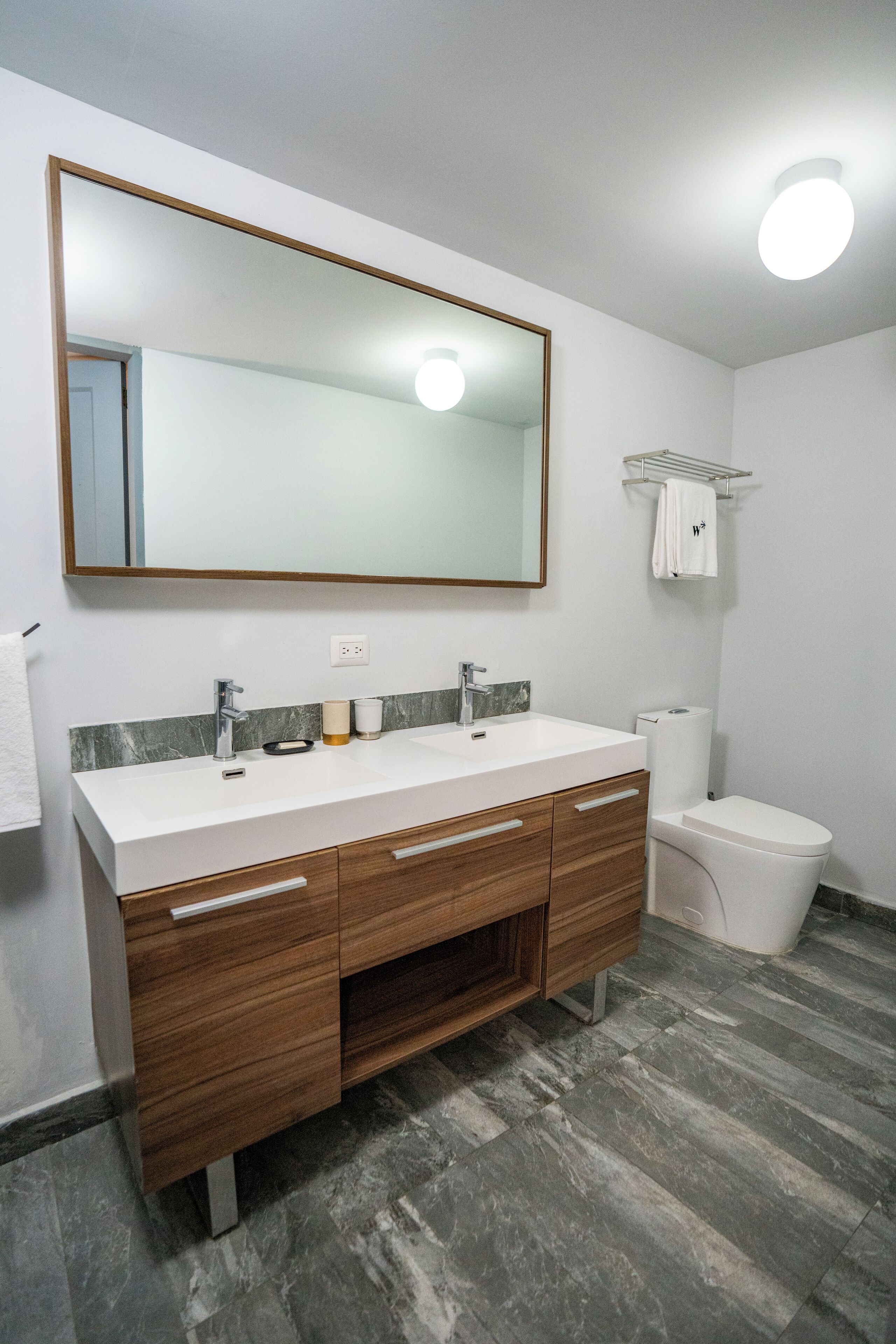 A modern bathroom with a white sink, wooden vanity, and a large mirror.