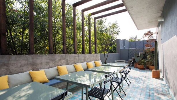 An outdoor seating area with tables and benches, surrounded by trees and potted plants.