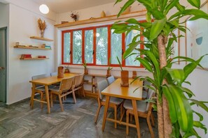 A dining area with wooden tables and chairs, a herringbone floor pattern, and a window with red frames.