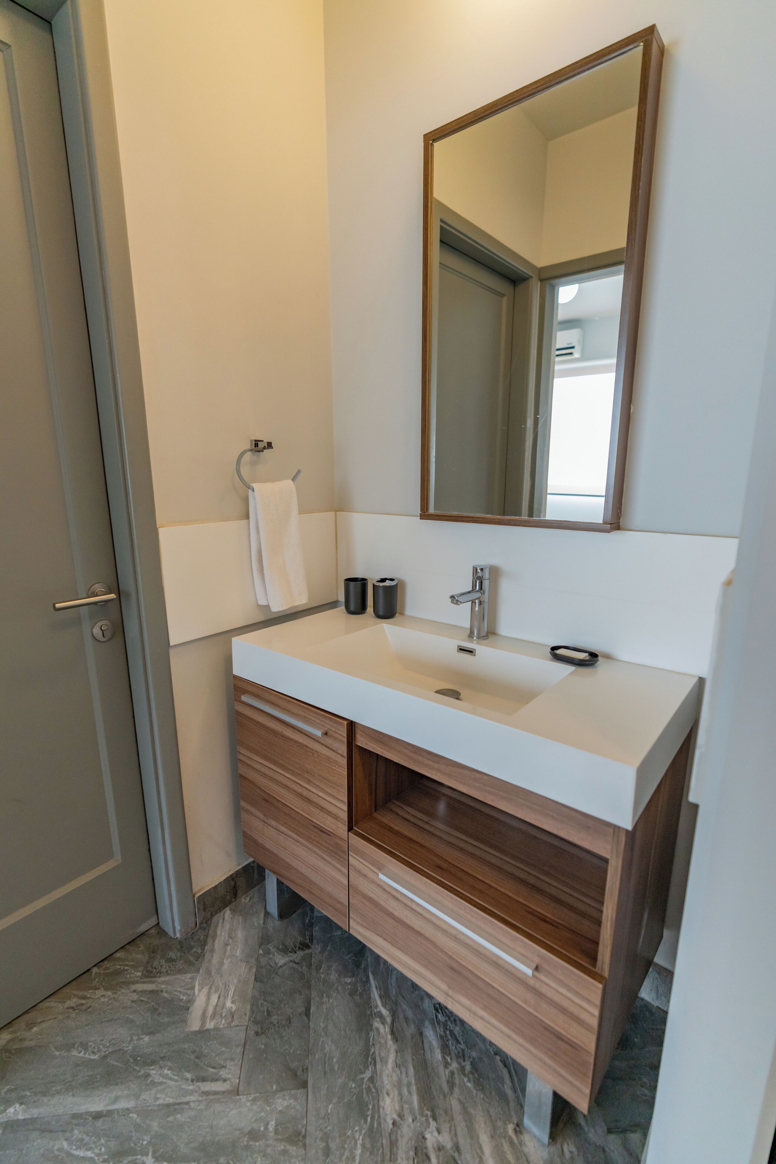 Un baño moderno con un lavamanos blanco, tocador de madera y un espejo grande.