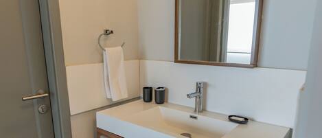 Un baño moderno con un lavamanos blanco, tocador de madera y un espejo grande.