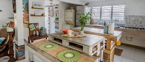 Una cucina con isola in legno, zona pranzo con una panca e piano cucina con lavello e fornello.