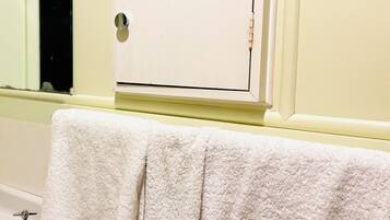 A bathroom with a white bathtub, a white towel hanging on the wall, and a white door with a window.