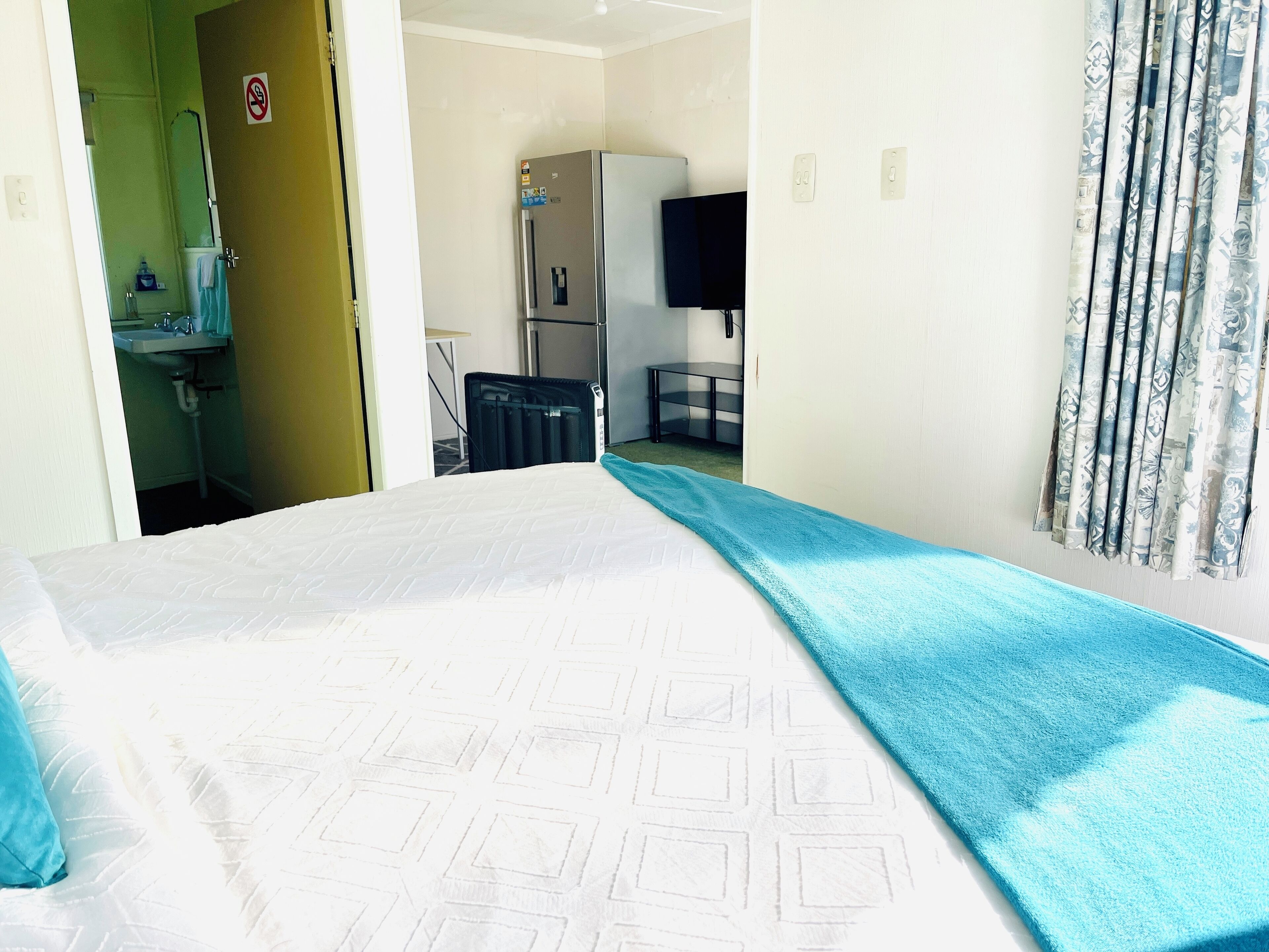 Ein Hotelzimmer mit Bett, Bad, Kühlschrank, Fernseher und Vorhang.