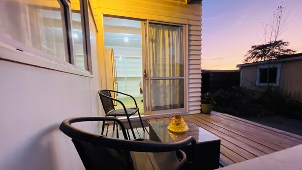 A patio with a table and chairs, a yellow decorative object, and a sliding glass door leading to a covered area. - Haven to Relax (Hamilton)