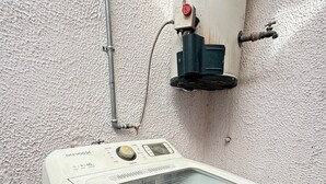 Une machine à laver blanche, dotée d’un panneau de commande, d’une arrivée d’eau et d’un tuyau raccordé à un réservoir d’eau.