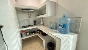 Une cuisine compacte équipée d’une cuisinière à gaz, d’un distributeur d’eau et de divers ustensiles de cuisine.