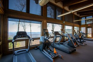 A gym with treadmills and elliptical machines, large windows with a mountain view, and wooden interior design. - Lucky Landing at Blue Ridge Mountain Club (Deep Gap)