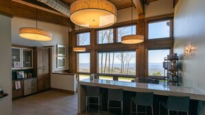 A modern kitchen with a large island, wooden beams, and large windows offering a view of the outdoors. - Lucky Landing at Blue Ridge Mountain Club (Deep Gap)