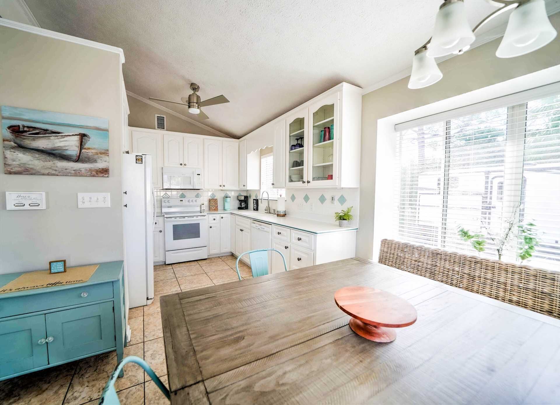 Une cuisine de taille réduite avec des meubles blancs, une table à manger en bois et un ventilateur de plafond.