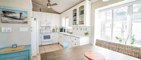 Une cuisine de taille réduite avec des meubles blancs, une table à manger en bois et un ventilateur de plafond.