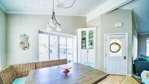 A dining area with a wooden table, wicker bench, and a glass cabinet with shelves. - 483 Marlin Dr. - Golf Cart & Beach Chair Service Included! (Panama City Beach)