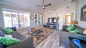 A spacious living room with two grey sofas, a coffee table, and a TV. - 483 Marlin Dr. - Golf Cart & Beach Chair Service Included! (Panama City Beach)