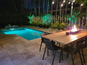 A swimming pool with a tiled deck, surrounded by palm trees and string lights. - SuCasa Palmas (Miami)