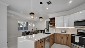 A modern kitchen with white cabinetry, a central island, stainless steel appliances, and pendant lighting. - SuCasa Palmas (Miami)