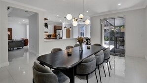 A modern dining area with a long table, grey upholstered chairs, and a contemporary chandelier. - SuCasa Palmas (Miami)