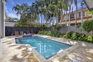 A rectangular swimming pool with a tiled edge, surrounded by a wooden fence and lush greenery. - SuCasa Palmas (Miami)