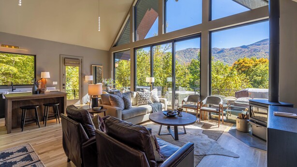A spacious living area with a large window overlooking a mountainous landscape, a cozy seating area, and a kitchen with a bar. - Big Bear Escape (Banner Elk)