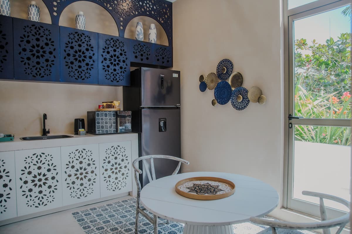 Una cocina funcional con refrigerador, gabinetes blancos y un comedor con mesa y sillas.