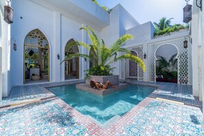 A pool area with a person relaxing, surrounded by white walls with arched doorways and decorative tiles. - Sana Tulum Beachfront Boutique Hotel (Tulum)