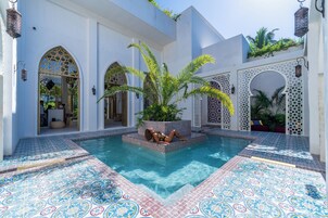 A pool area with a person relaxing, surrounded by white walls with arched doorways and decorative tiles.
