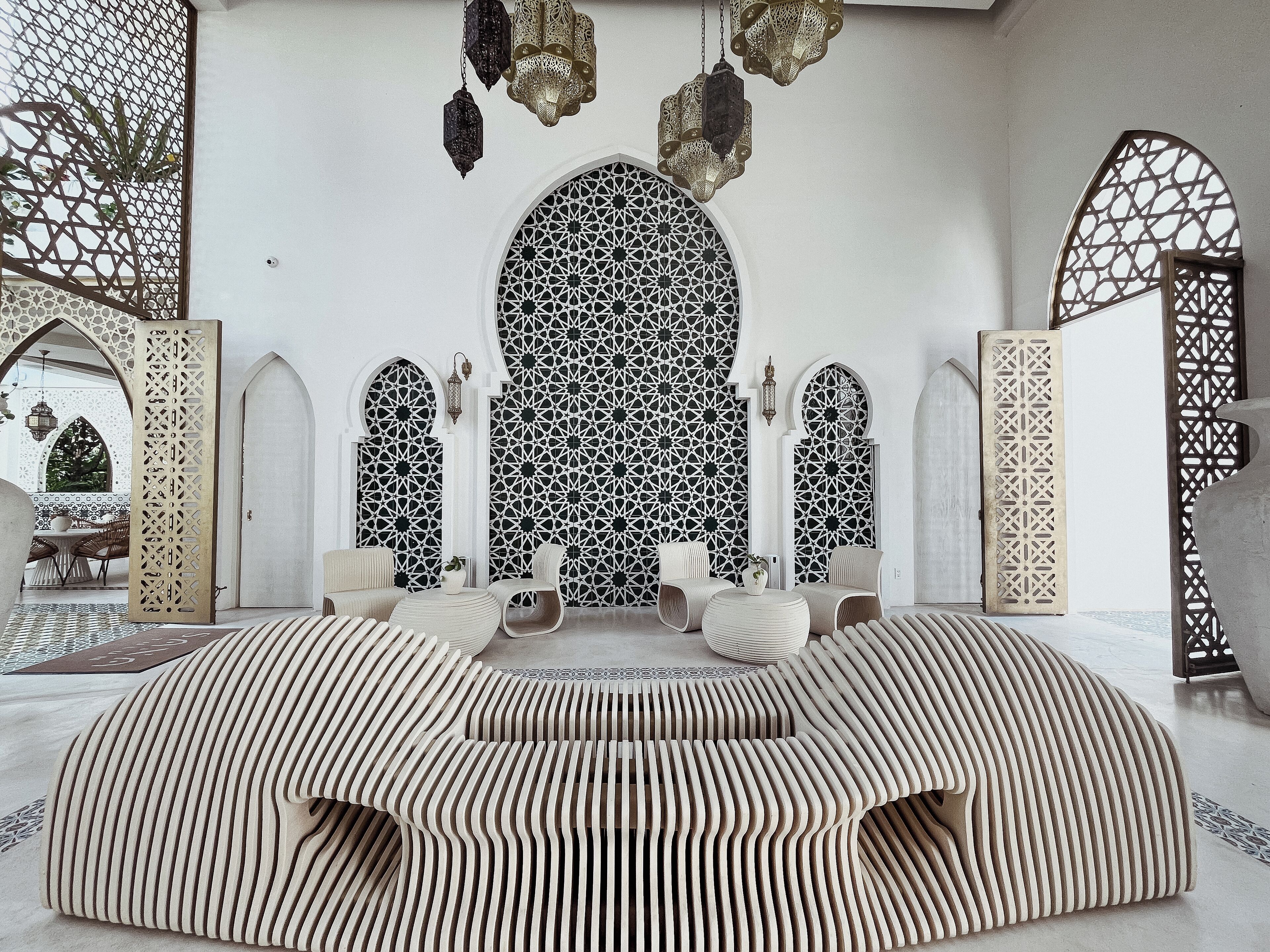 A room with a patterned wall, a seating area with cushions, and hanging lanterns.