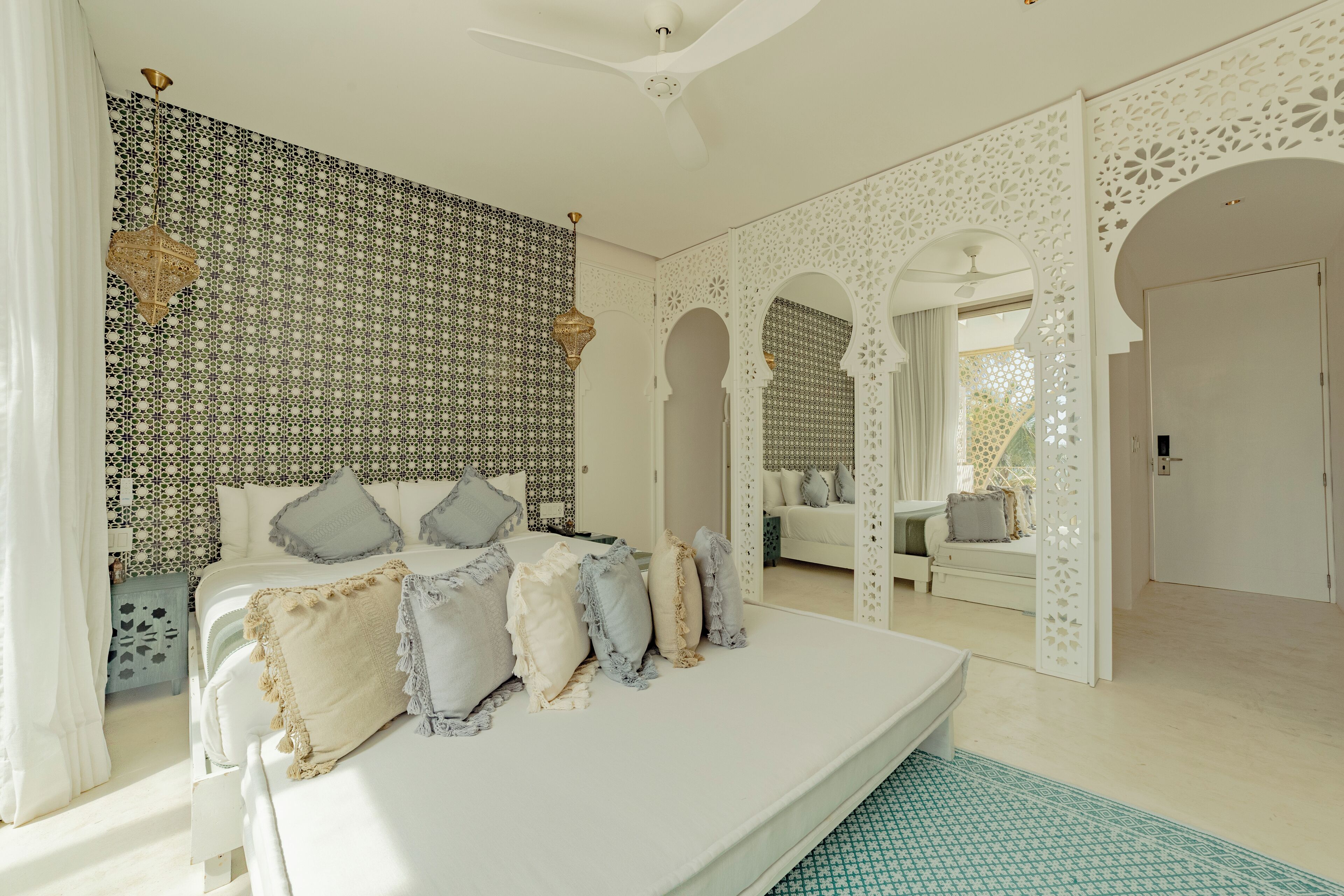 A bedroom with a large bed, patterned wallpaper, and a decorative ceiling fan.