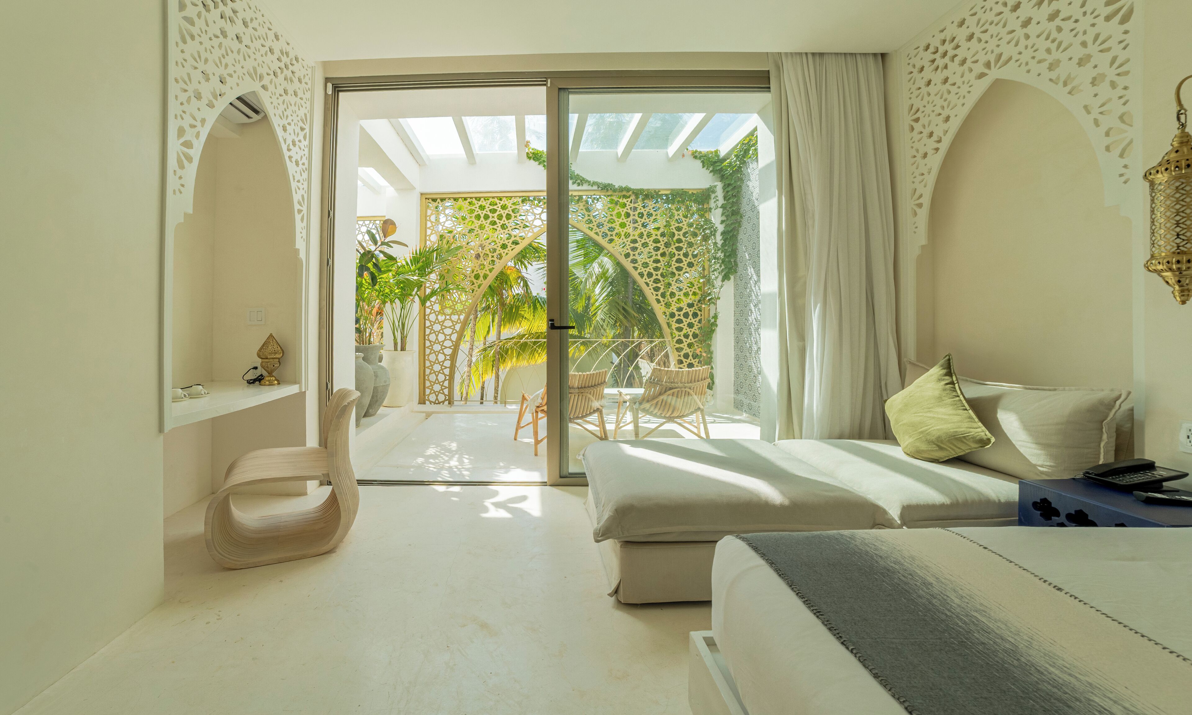 A modern hotel room with a balcony, a bed, a seating area, and a view of the outdoors.