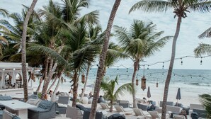 A beachside lounge with outdoor seating, palm trees, and a view of the ocean. - Sana Tulum Beachfront Boutique Hotel (Tulum)