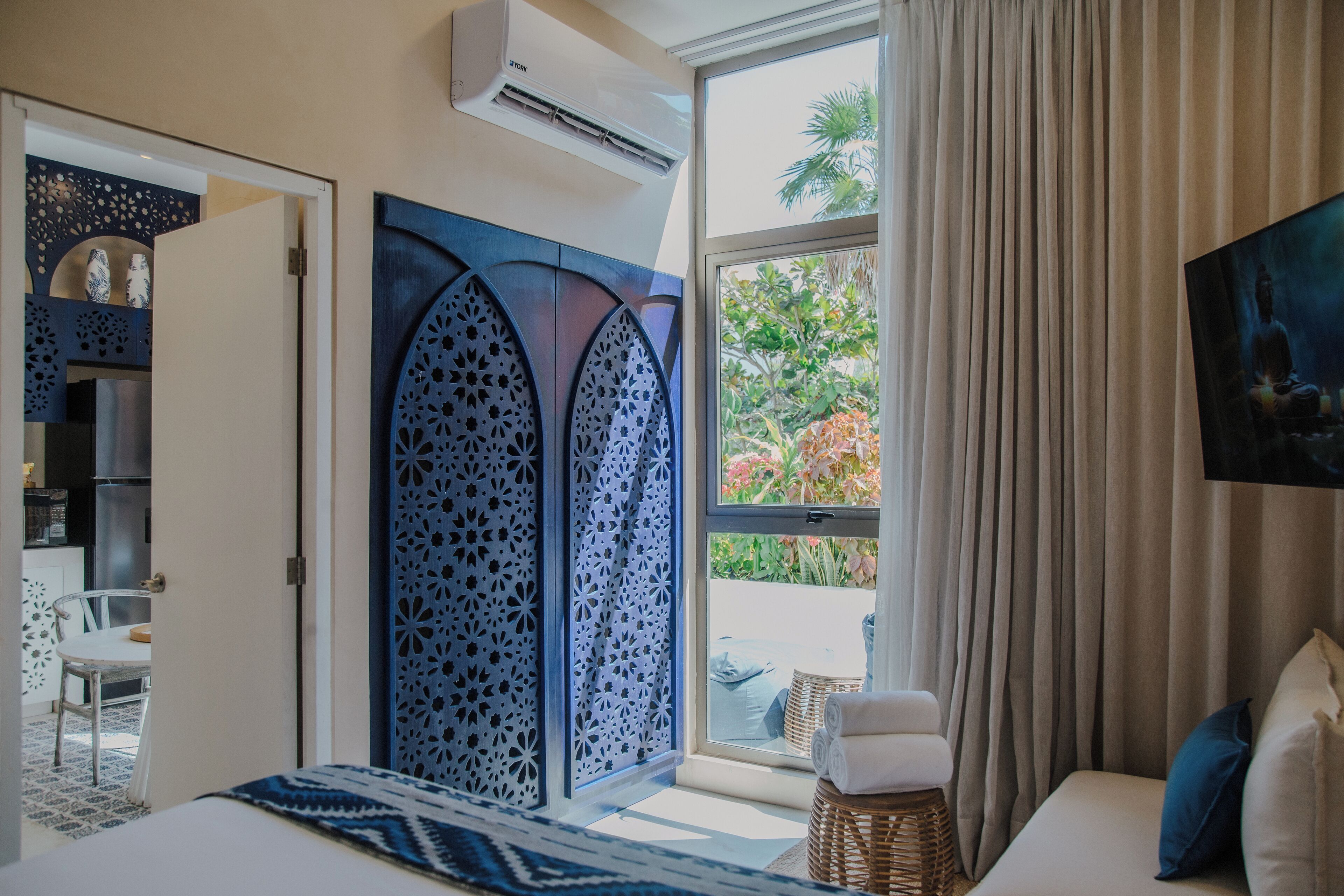 A bedroom with a bed, a window with curtains, a TV mounted on the wall, and a view of the outdoors.