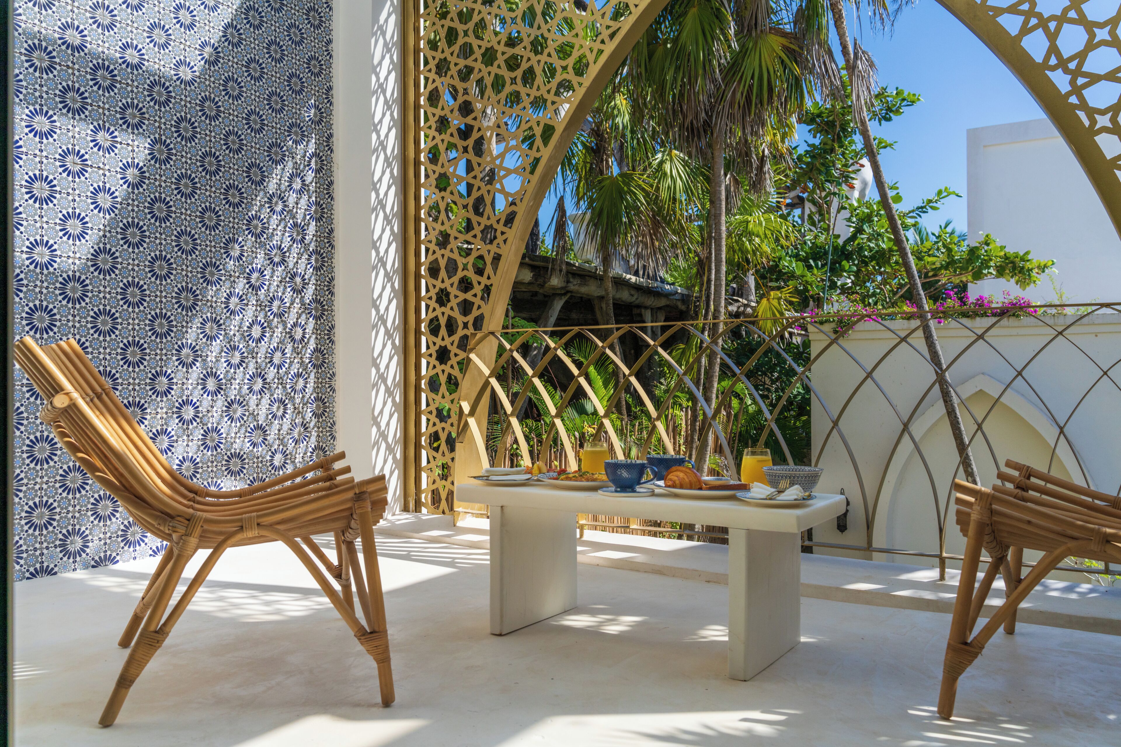 A patio with two wicker chairs, a table with dishes, and a decorative wall with a geometric pattern.
