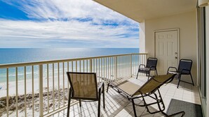 A balcony with a view of the ocean, equipped with two wicker chairs and a table.