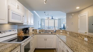 A kitchen with white cabinets, granite countertops, a built-in oven, and a stainless steel sink.