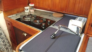 A compact kitchenette with a gas stove, a sink with a faucet, and cabinets above. - Alojamento Barco Casa Ancorado no Coração da Ria Formosa em Faro (Faro)