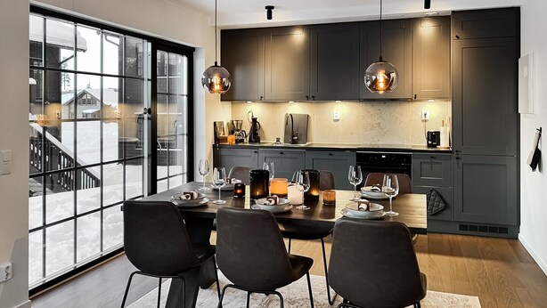 A modern kitchen with dark cabinets, a dining table set for four, and pendant lighting.