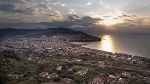 Une vue aérienne d’une ville côtière, avec un mélange de bâtiments résidentiels et commerciaux, une étendue d’eau importante et un paysage vallonné en arrière-plan.