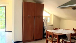 Une pièce avec une armoire en bois, une table à manger avec des chaises, et une vue sur la verdure par une porte.