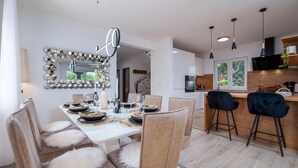 A modern dining area with a white table set for four, surrounded by plush chairs with white fur throws. A decorative mirror and geometric wall art adorn the space. - Beautiful home in Pula (Pula)