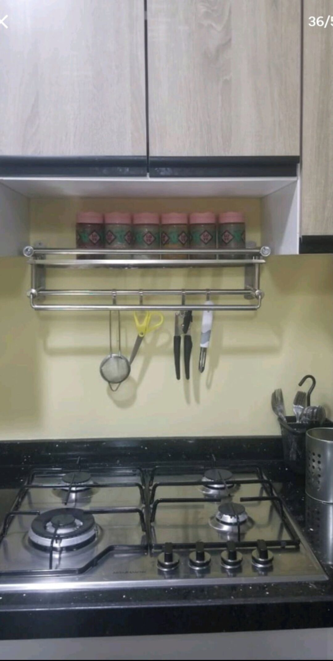 A kitchen with a gas stove, a metal rack above the stove holding kitchen utensils, and a shelf with jars.