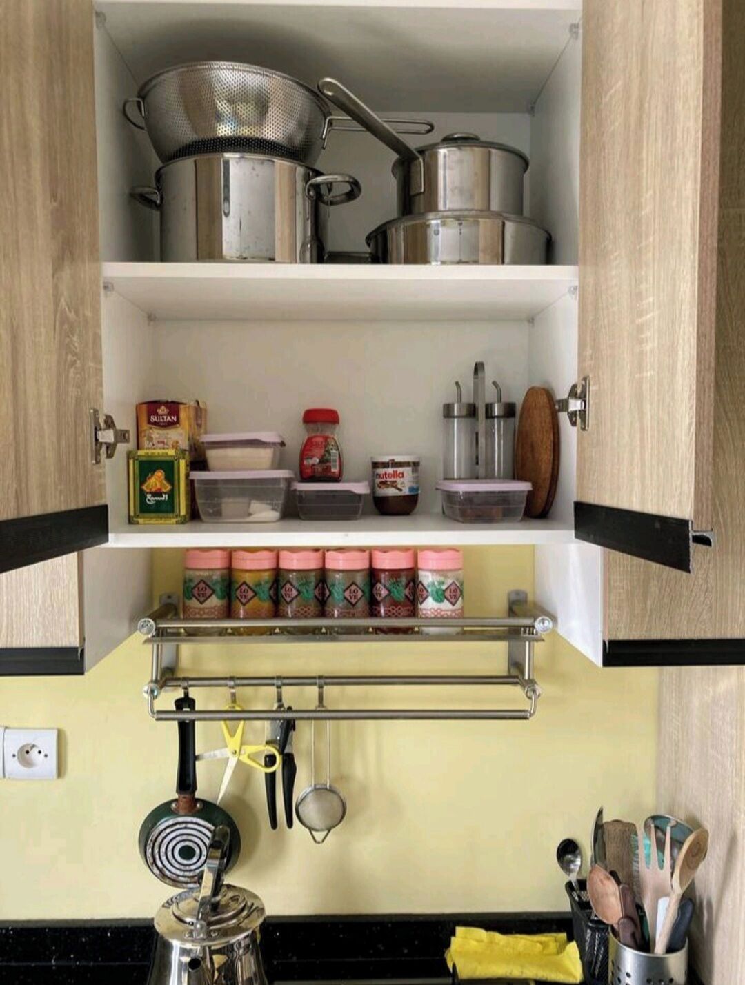 A kitchen with stainless steel pots, a colander, a spice rack, and utensils.