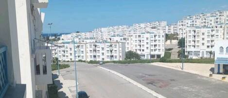 A residential area with white apartment buildings, a clear blue sky, and a road with parked cars.