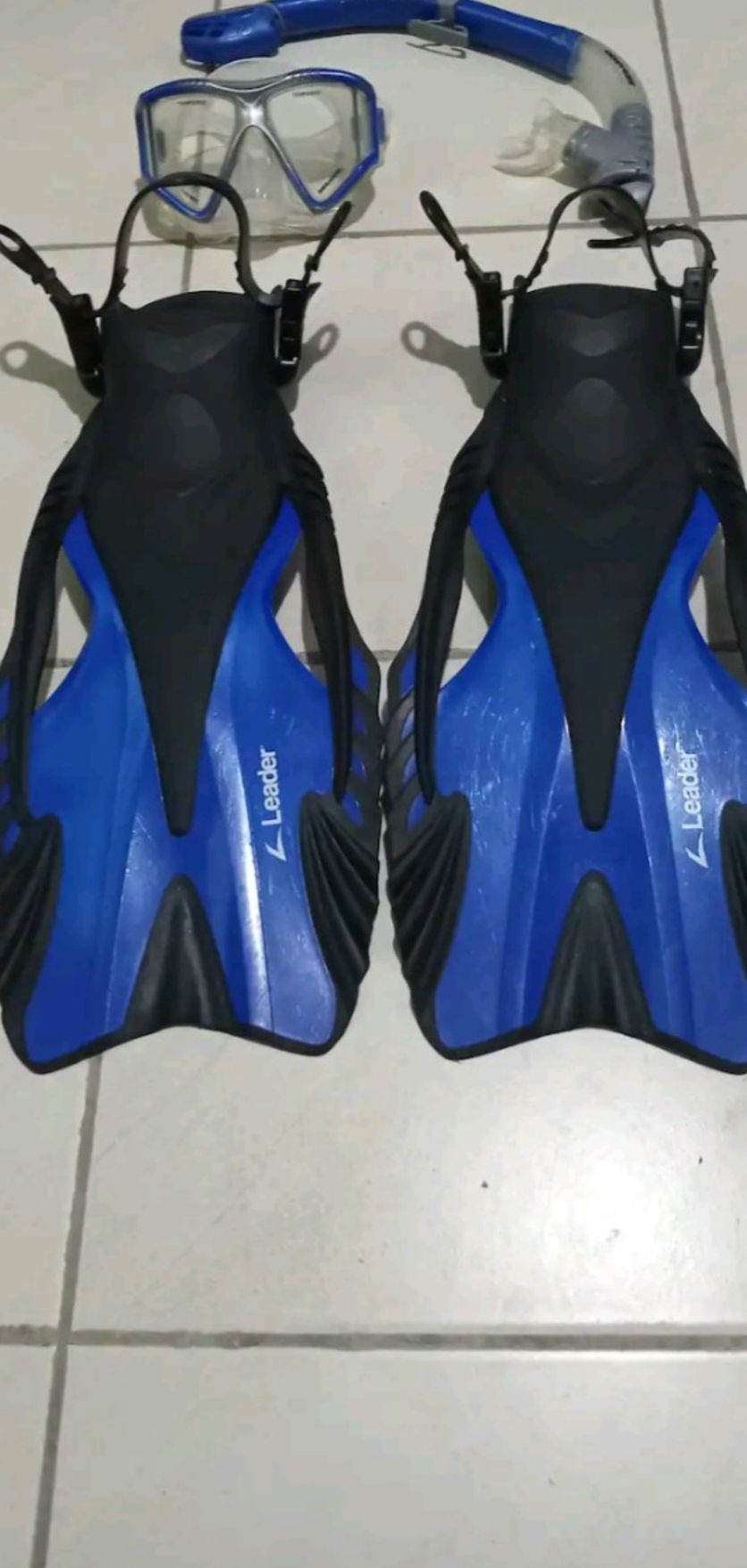A pair of blue and black diving fins with the brand name 'Leander' on them, placed on a tiled floor.
