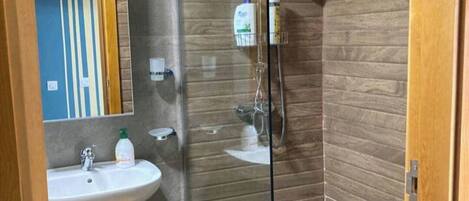 A bathroom with a glass shower enclosure, a sink with a mirror, and toiletries on the wall.