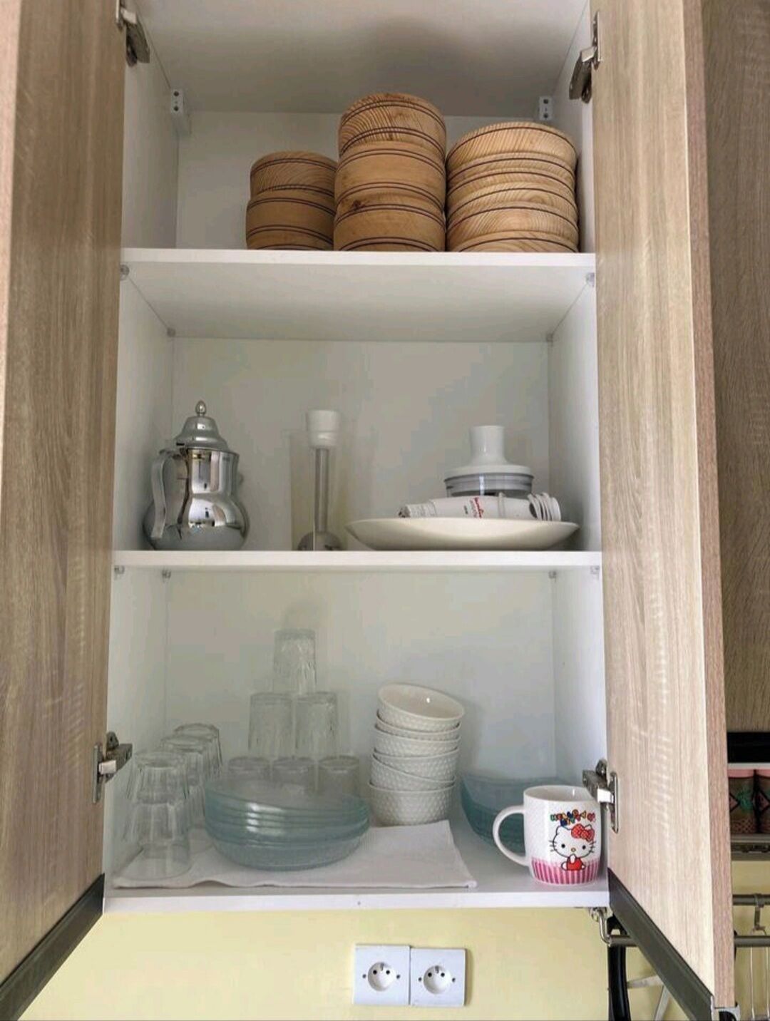 A kitchen cabinet with three shelves, each containing different items.
